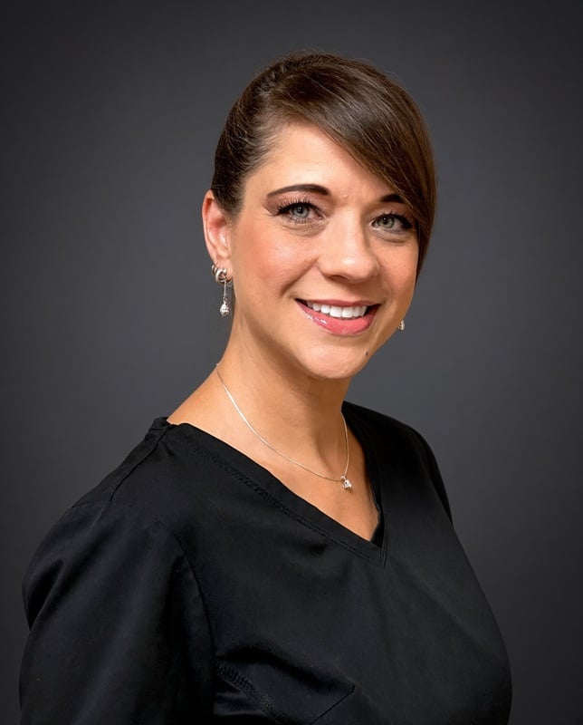 Headshot of a smiling female staff member with brunette hair styled in a side-swept bang wearing a black top