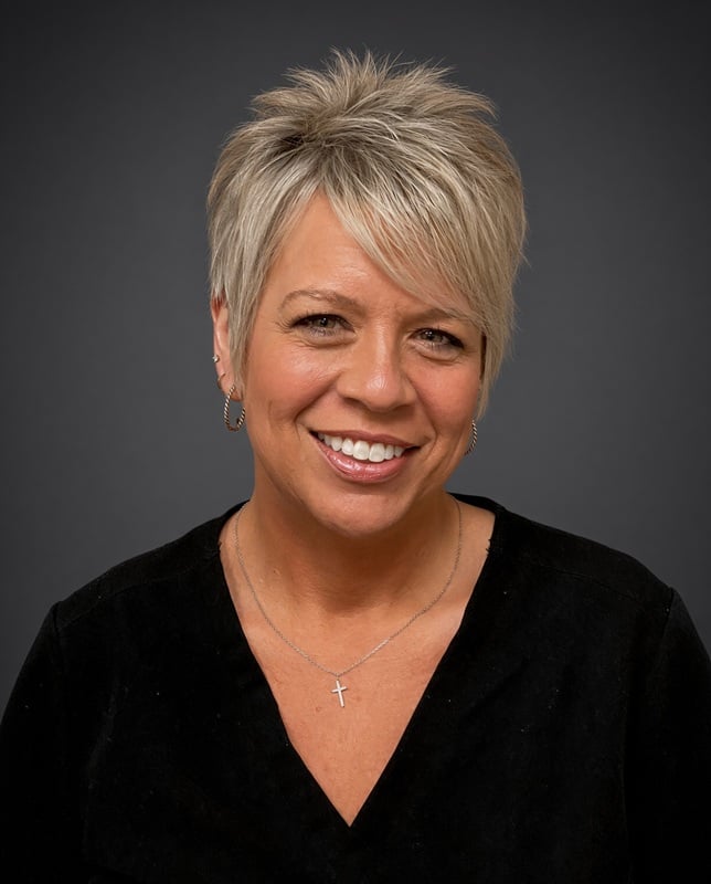 Headshot of a smiling female staff member with short blonde hair wearing a black top against a studio backdrop