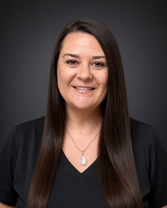 Headshot of a smiling female staff member with long straight dark hair wearing black scrubs and a drop necklace