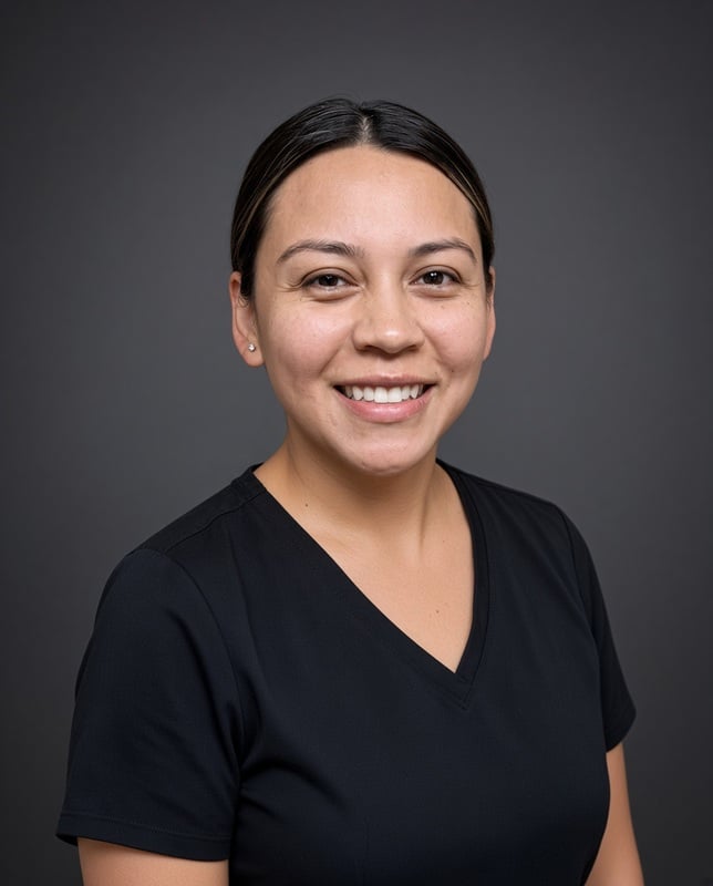 Headshot of a smiling female staff member with dark hair pulled back into a ponytail wearing black scrubs