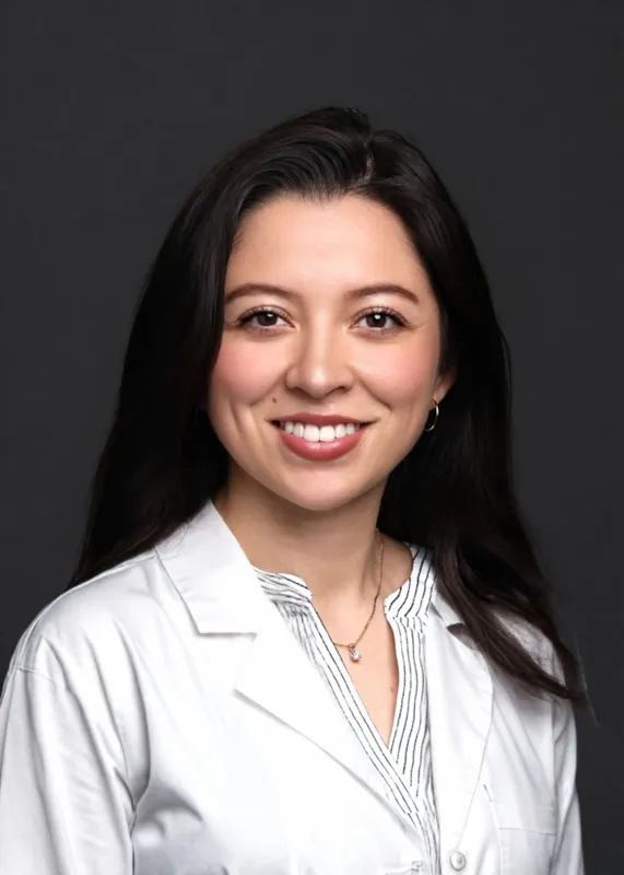 Headshot of Dr. Melissa Sierra smiling in a white lab coat against a dark grey background