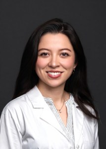 Headshot of Dr. Melissa Sierra smiling in a white lab coat against a dark grey background